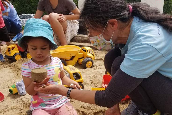 Toddler and staff member playing in a sandbox