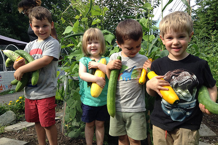 Children holding squash and zucchini in the garden